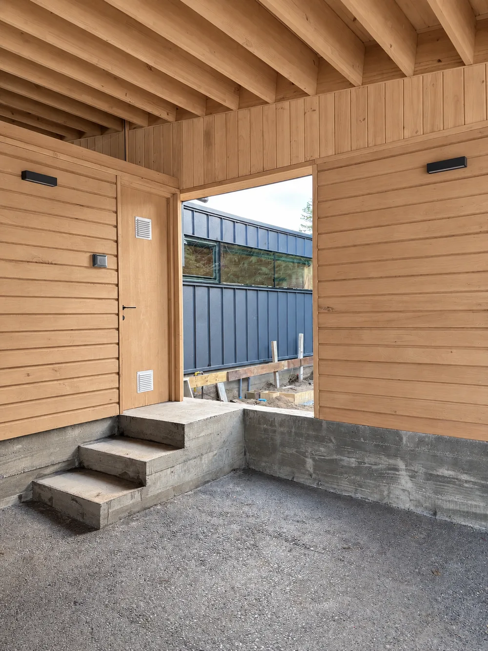Casa Almares — acceso lateral con peldaños de hormigón entre revestimientos de madera y metal