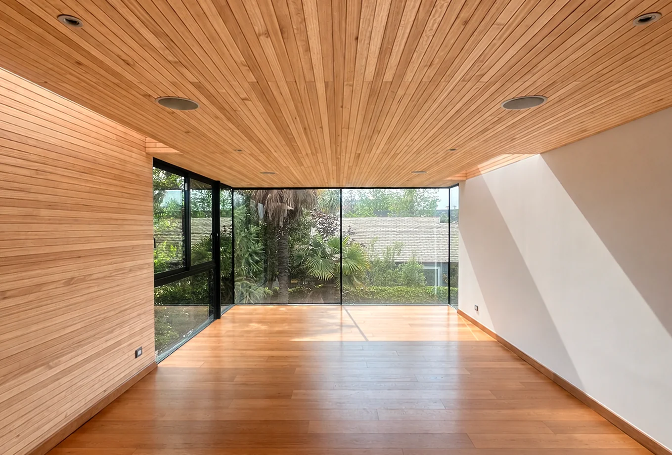 Casa Buenaventura — sala revestida en madera con ventanal esquinero hacia el jardín