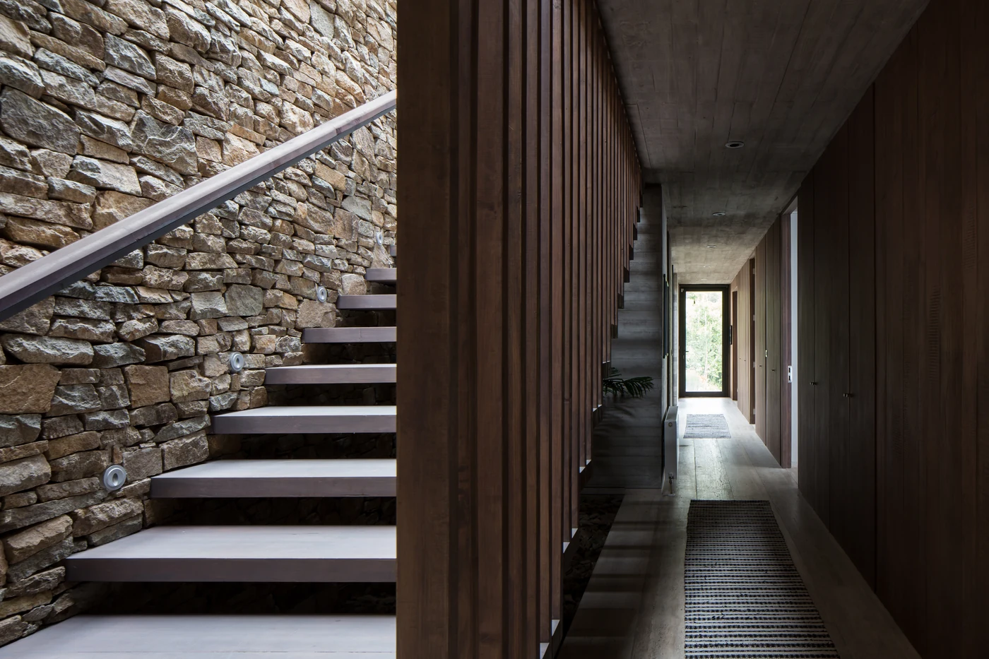 Casa 59 — pasillo interior con muro de piedra y consola de madera