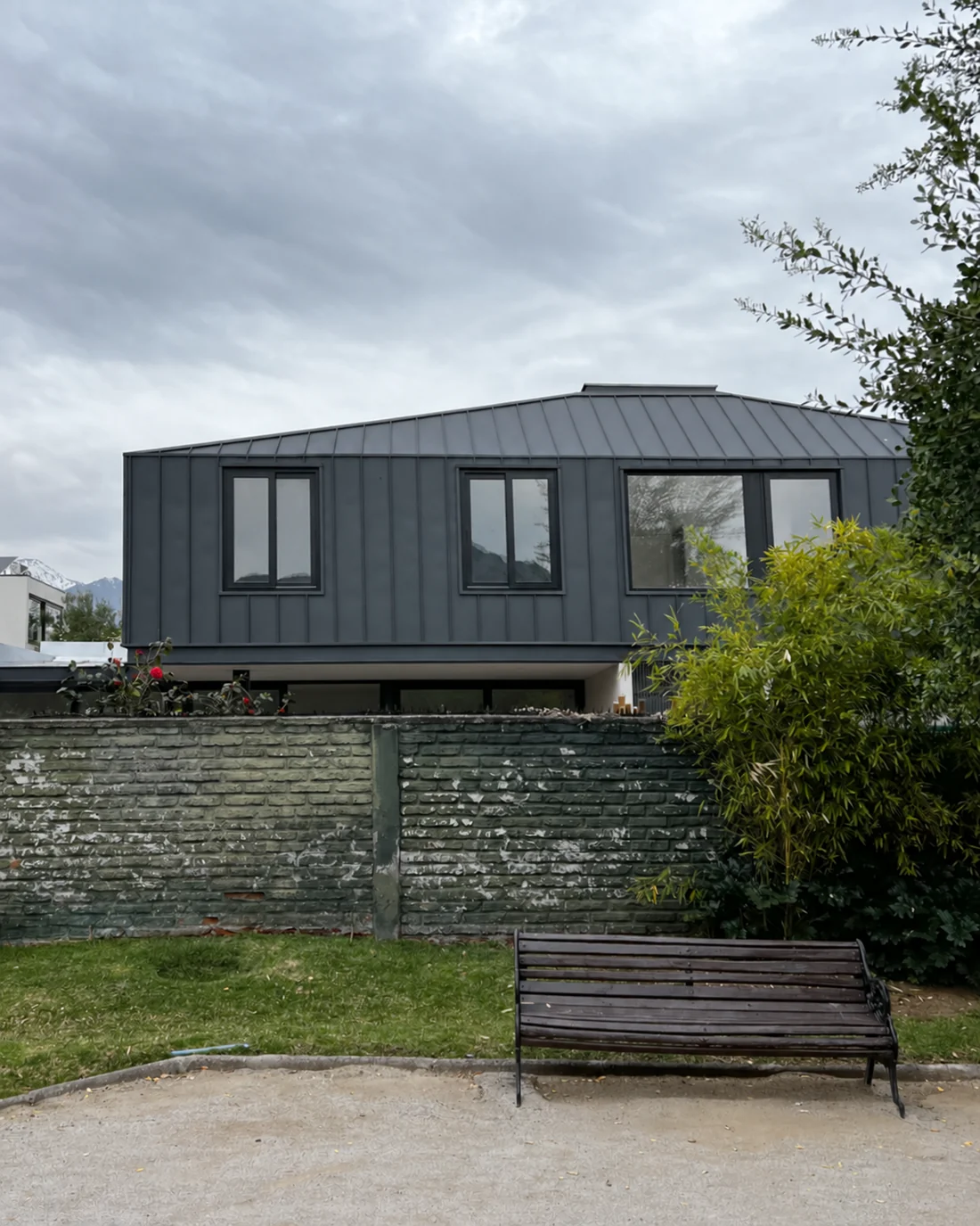 Casa Apolo — fachada con volumen de metal oscuro sobre muro de albañilería y jardín