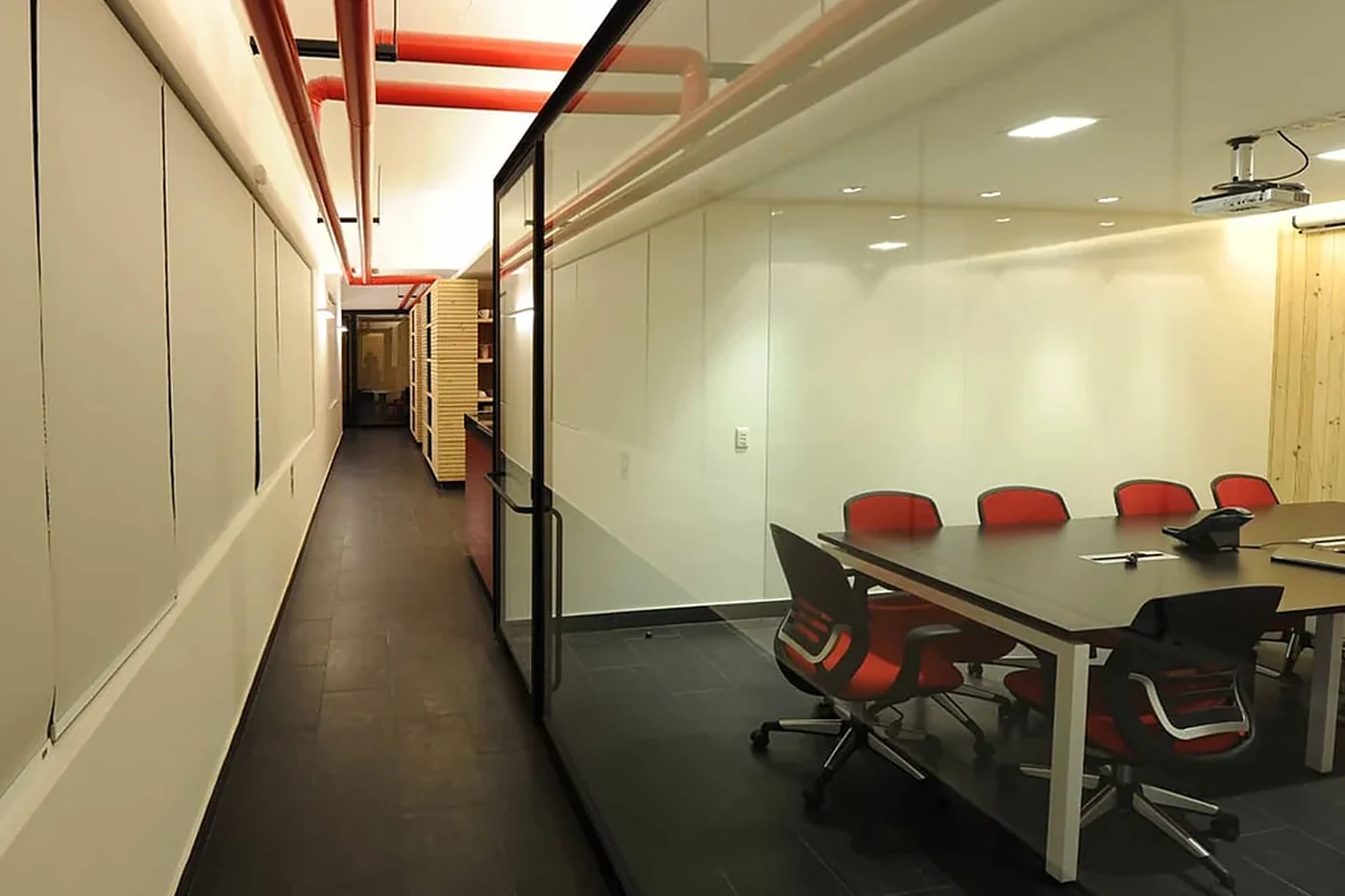 Casa Ideas — pasillo a la sala de reuniones, con tuberías rojas a la vista