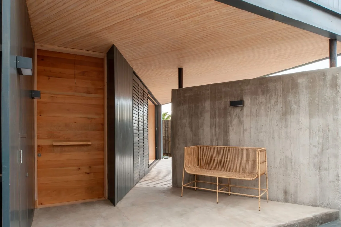 Casa Laguna — entrada principal con cielo de madera, muro de hormigón y banca