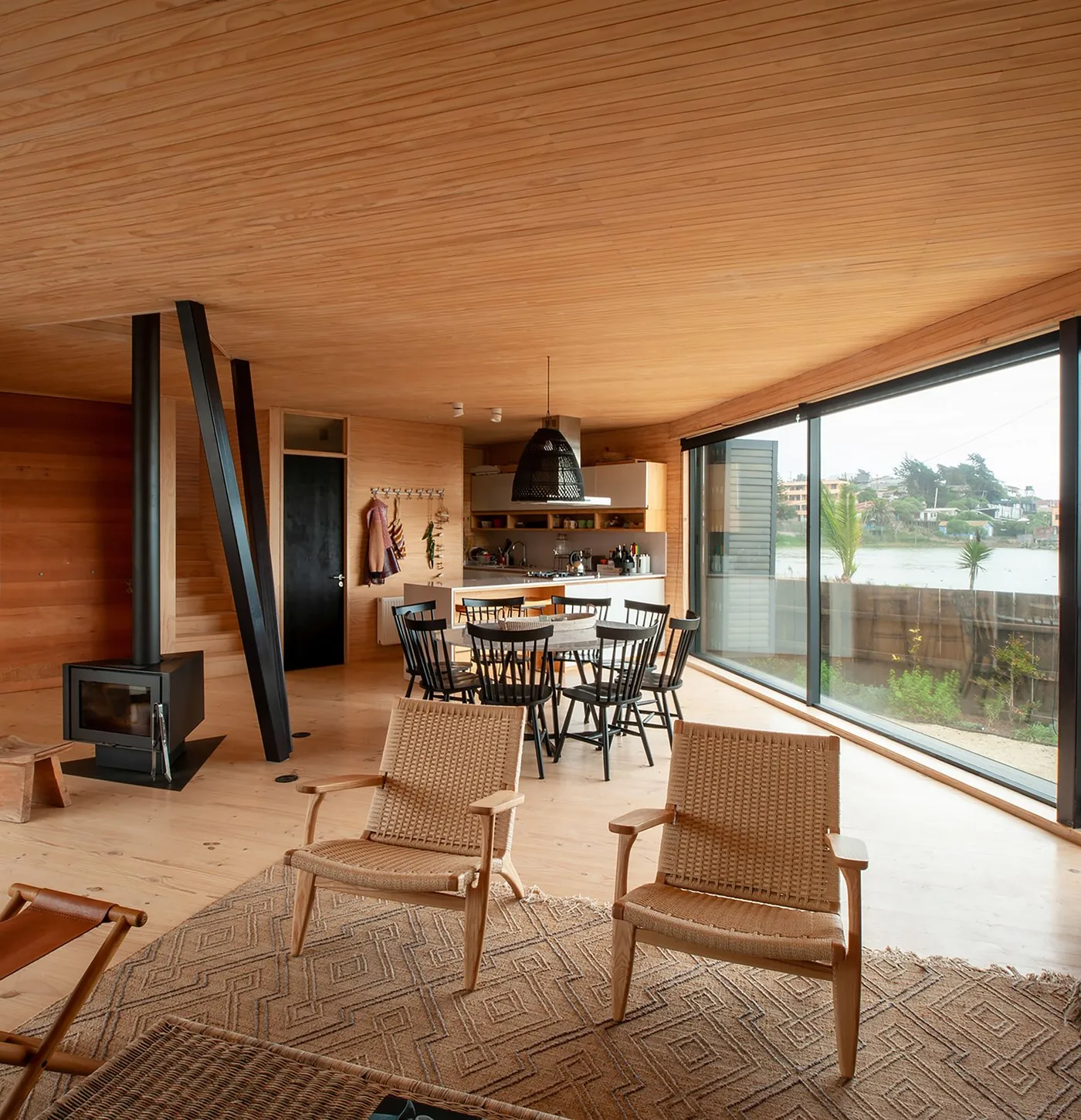 Casa Laguna — living-comedor de madera con vista a la laguna y la chimenea de acero
