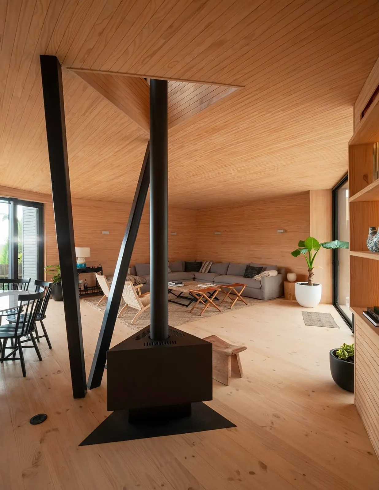 Casa Laguna — living interior de madera con la chimenea de acero y la estructura diagonal, iluminado por la lucarna