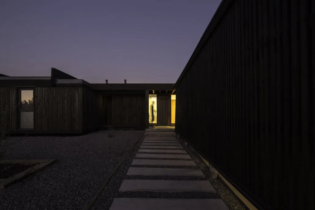 Casa TH — acceso peatonal nocturno, sendero de piedra hacia la entrada iluminada