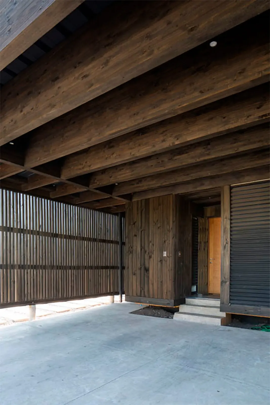 Casa TH — detalle del carport: vigas de madera laminada y revestimiento de madera quemada