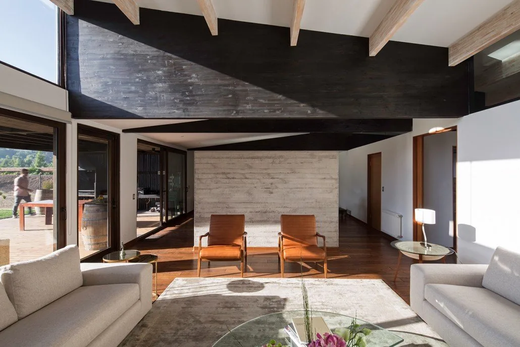 Casa TH — estar interior con grandes vigas de madera laminada, cielo oscuro y muro de hormigón