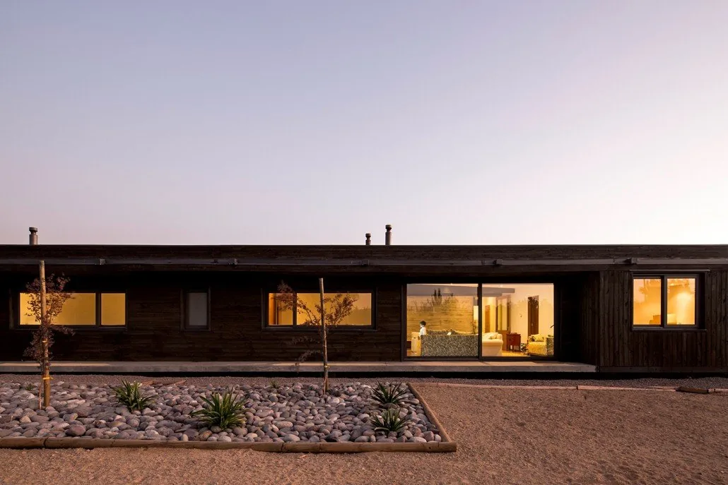 Casa TH — fachada lineal al atardecer con ventanas iluminadas y jardín de piedras