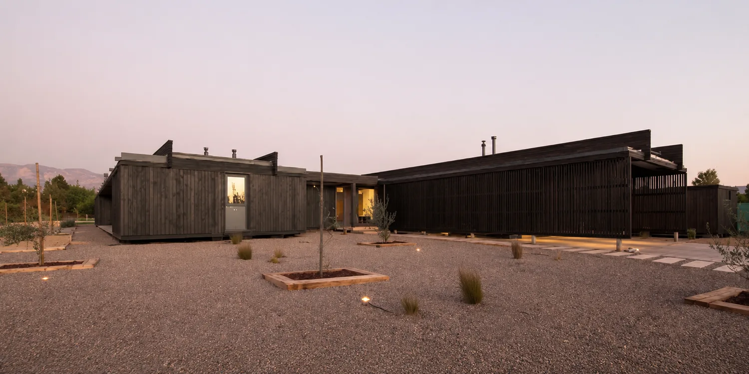 Casa TH, Chicureo — vista general de la vivienda al atardecer, dos cuerpos longitudinales revestidos en madera