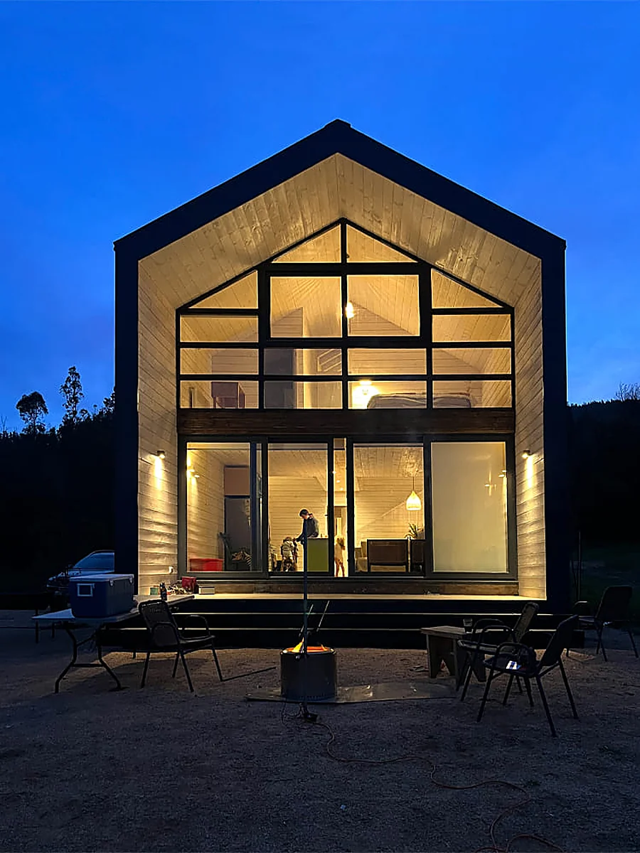 Casa VG — fachada principal iluminada al anochecer, el ventanal de la testera brillando como una linterna