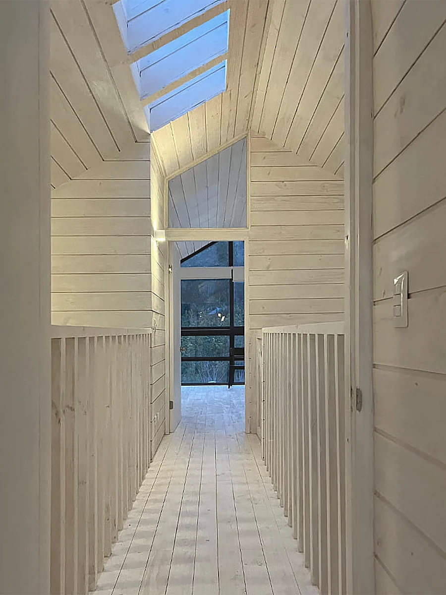 Casa VG — pasillo interior de madera con lucarna cenital y ventanal en la testera