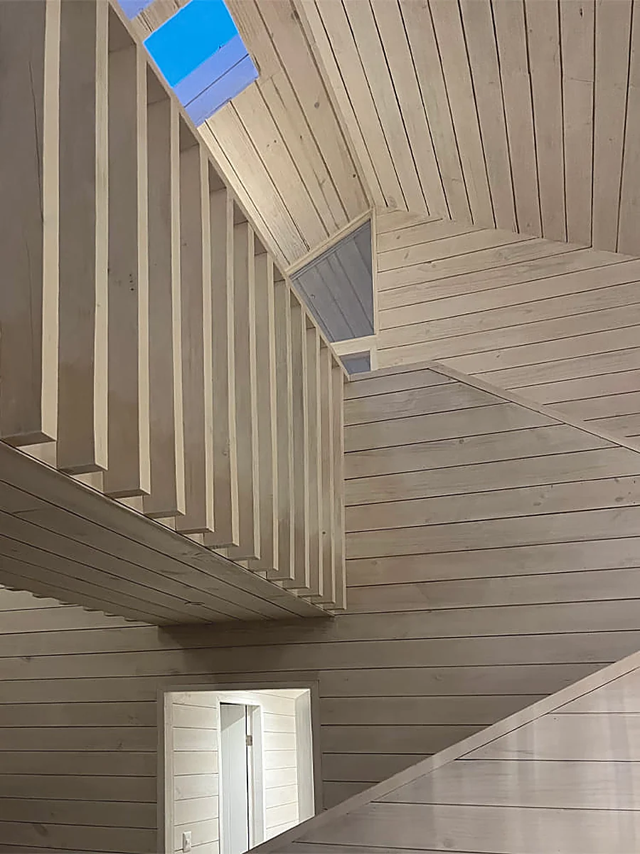 Casa VG — vacío interior a doble altura, revestido en madera blanquecina, con lucarna cenital