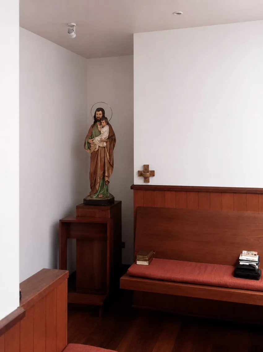 Oratorio — imagen religiosa sobre pedestal de madera junto a las bancas